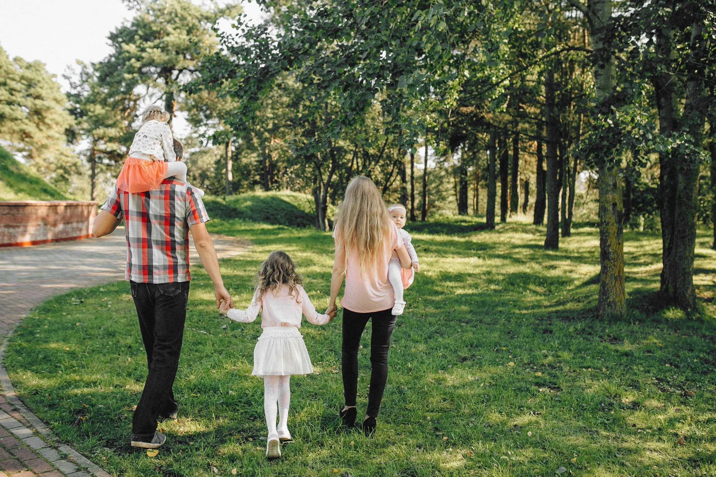 Familia de espaldas caminando de la mano por un parque con luz entre los árboles.