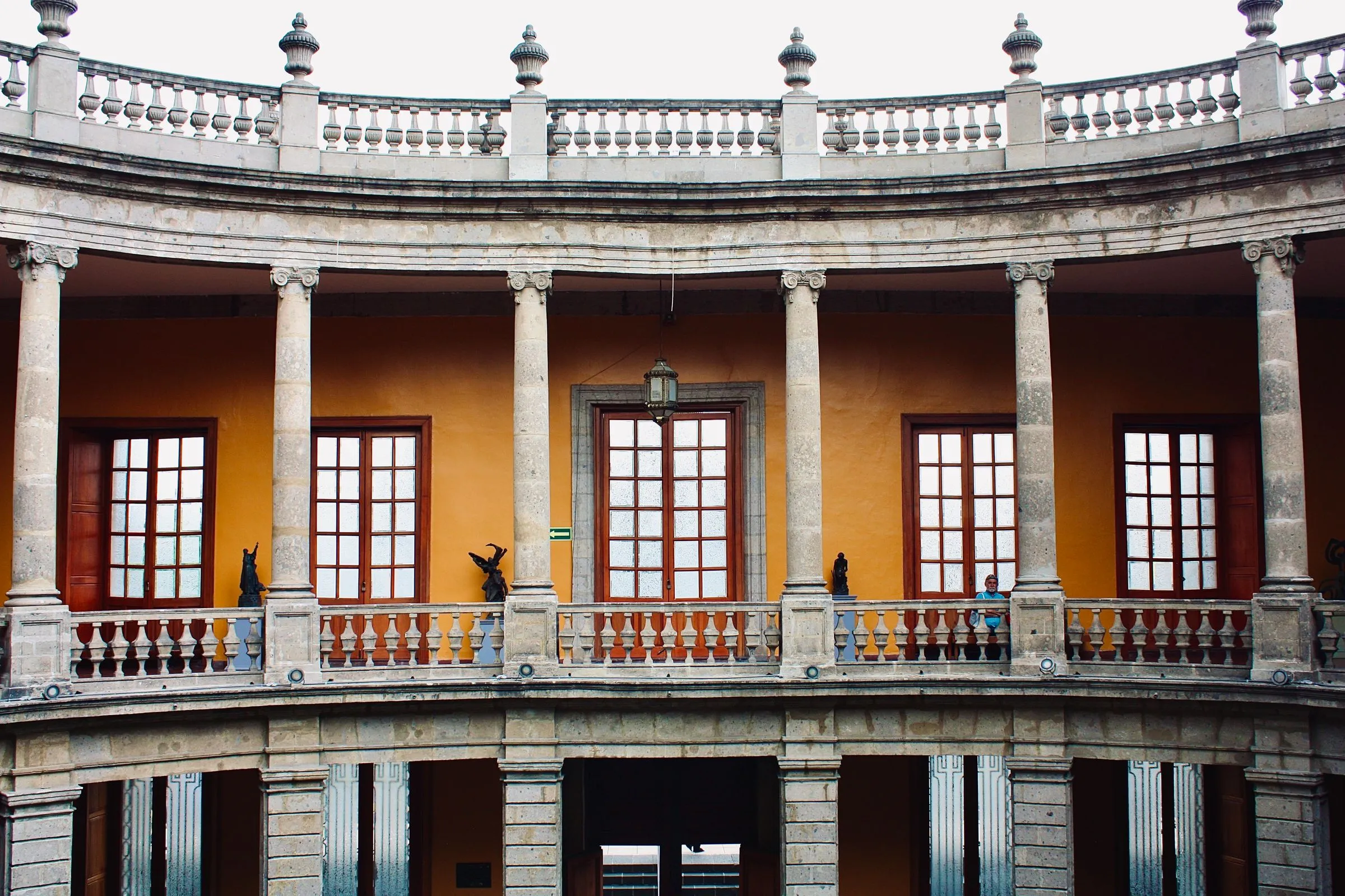 Patio de un edificio histórico en la Ciudad de México con columnas de cantera, balcones y ventanas de madera sobre muros ocre.