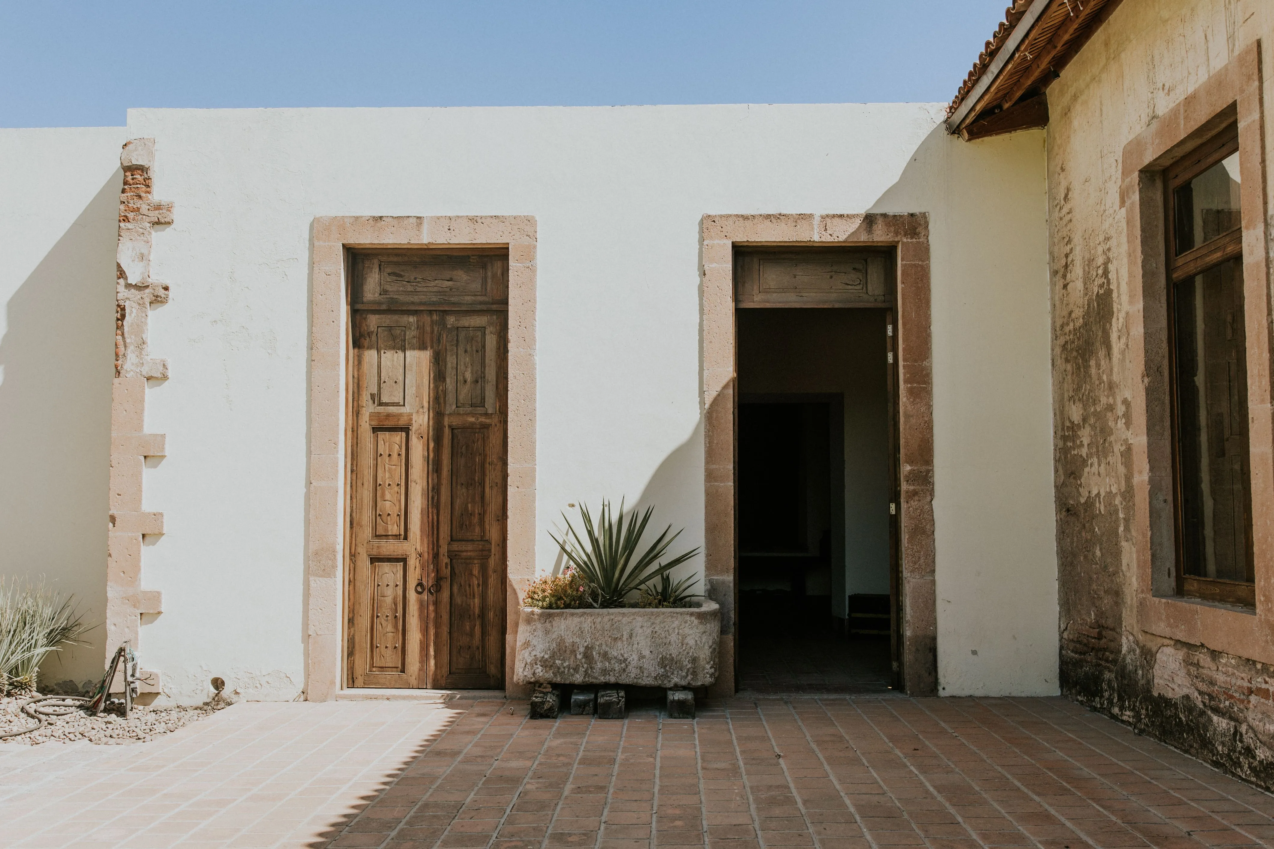 Patio con dos puertas de madera enmarcadas en cantera y piso de barro, a plena luz.