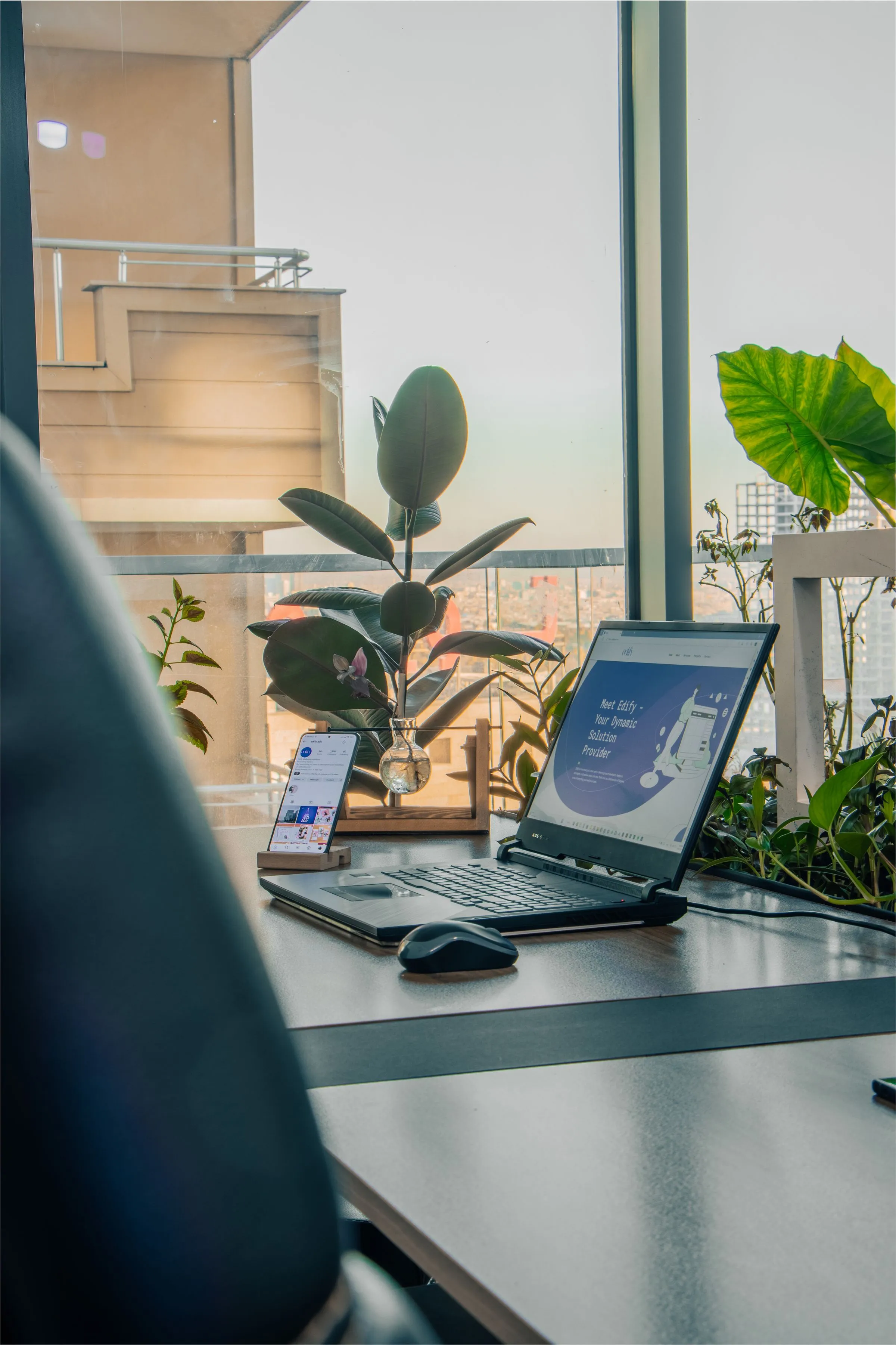 Laptop sobre un escritorio junto a un ventanal con plantas.